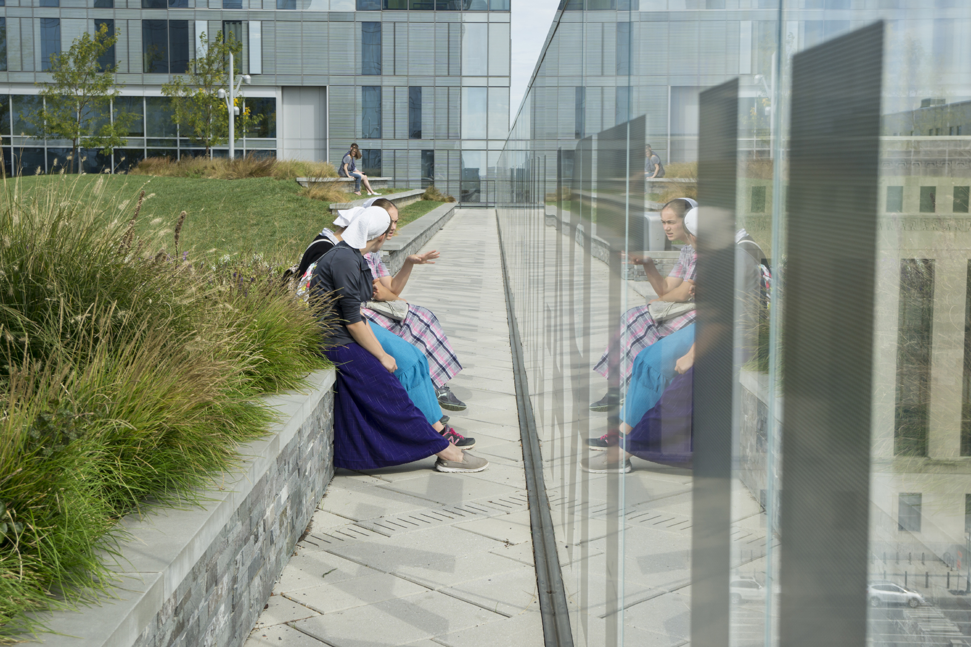 Young women sitting on wall next to reflecting wall