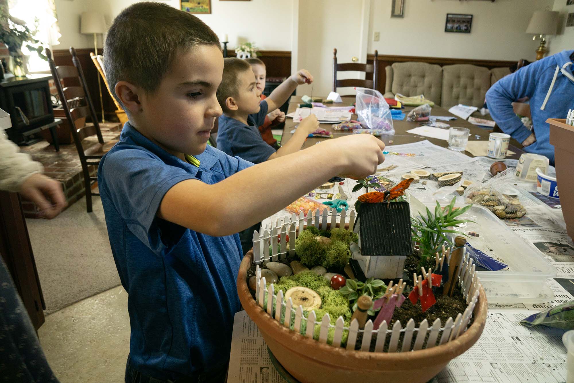 Boy in a blue shirt working on fairy garden in terra cotta pot.