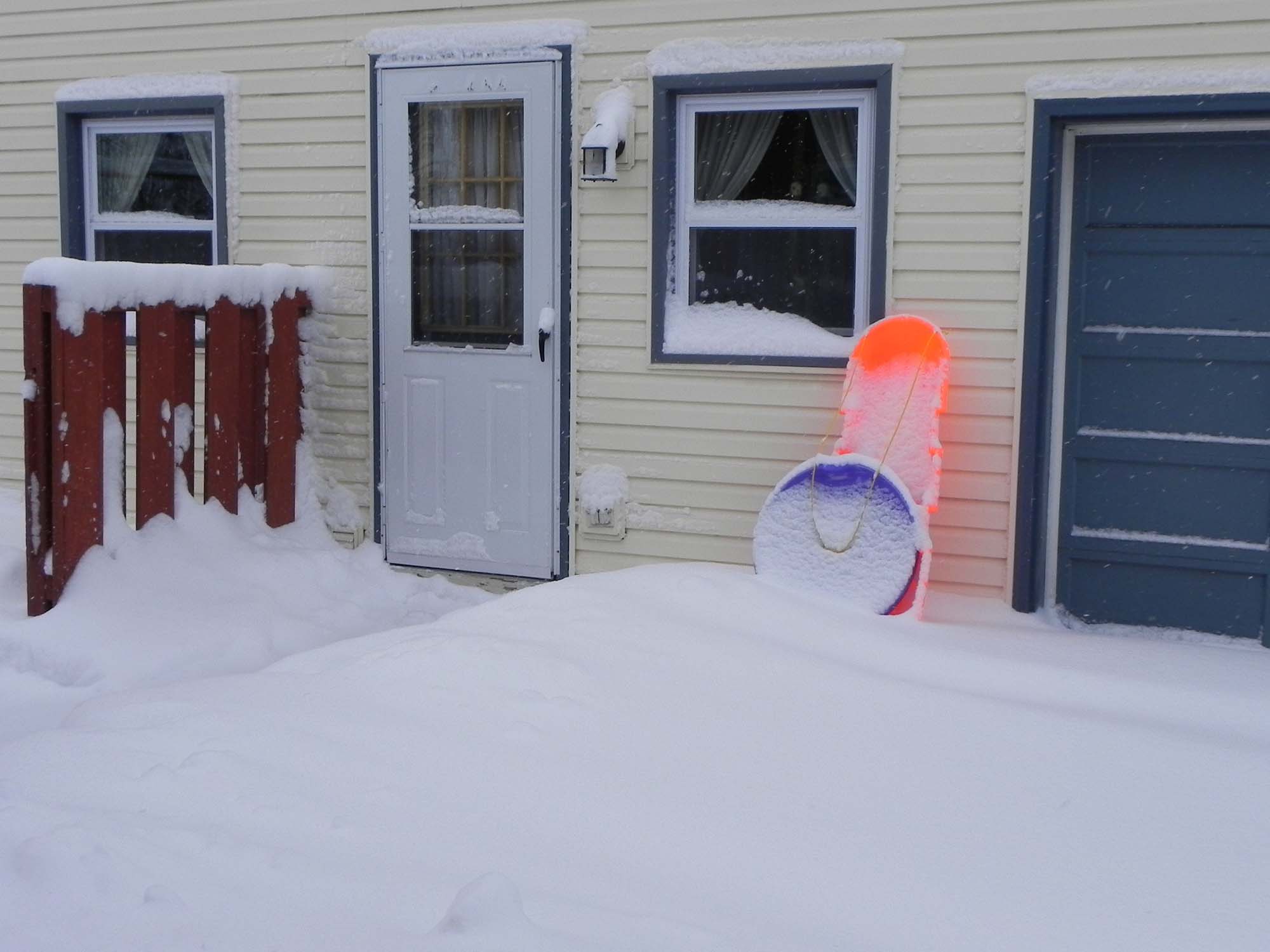 Two plastic sleds leaning against house in snow.